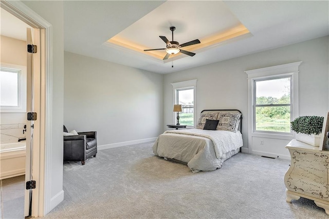 bedroom featuring multiple windows, ensuite bathroom, light colored carpet, and a tray ceiling