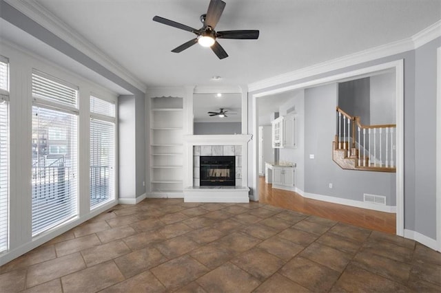 unfurnished living room featuring a tile fireplace, ceiling fan, crown molding, and built in shelves