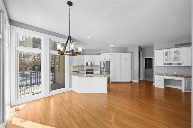 kitchen with pendant lighting, hardwood / wood-style flooring, appliances with stainless steel finishes, white cabinetry, and built in desk