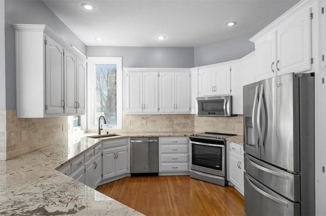 kitchen featuring white cabinetry, stainless steel appliances, light stone countertops, and sink