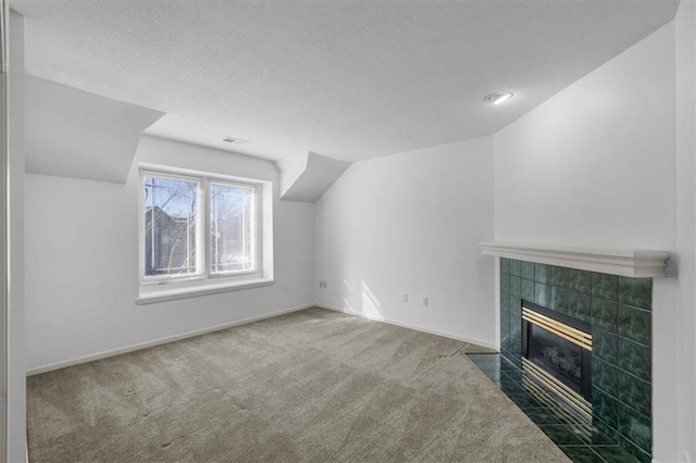 unfurnished living room featuring a tiled fireplace, lofted ceiling, carpet, and a textured ceiling