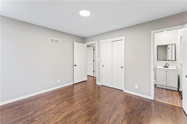 unfurnished bedroom featuring ensuite bath, sink, dark hardwood / wood-style flooring, and a closet