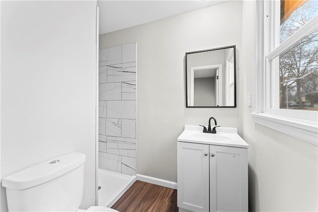 bathroom featuring wood-type flooring, tiled shower, vanity, and toilet