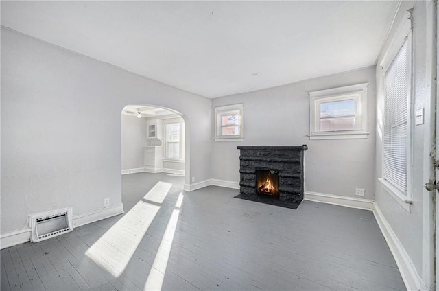 2463 Denver Ave, Kansas City, MO 64127 - unfurnished living room with a fireplace with flush hearth, dark wood-style floors, healthy amount of natural light, and arched walkways