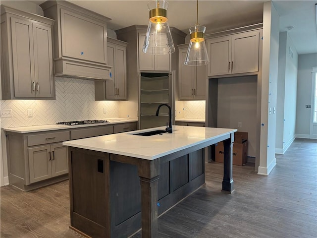 kitchen featuring decorative light fixtures, a center island with sink, custom range hood, light countertops, and a sink