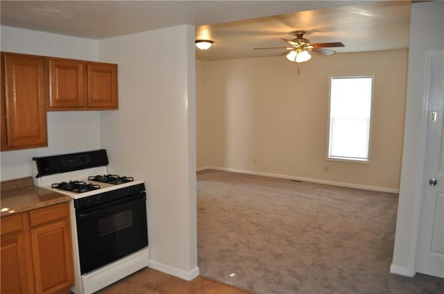 kitchen featuring range with gas cooktop, light colored carpet, and ceiling fan