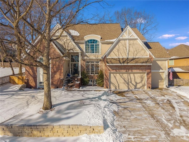 view of front of home with driveway, brick siding, an attached garage, fence, and stucco siding