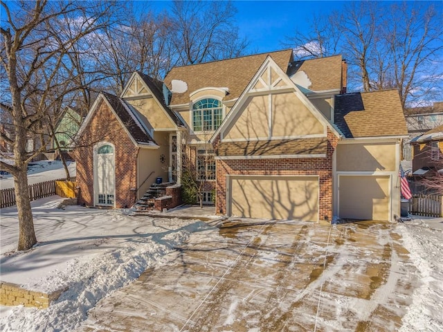 tudor home with a garage, brick siding, fence, and stucco siding