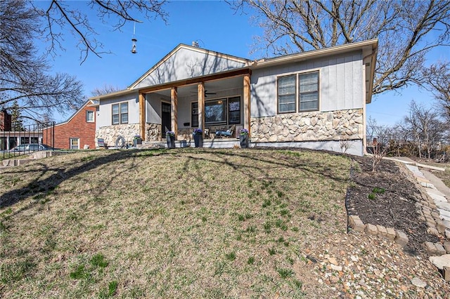 back of property with board and batten siding, a ceiling fan, stone siding, and a lawn