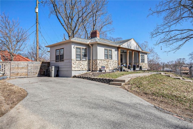 view of front of home with aphalt driveway, fence, stone siding, and a chimney