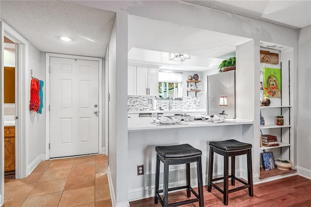 kitchen with a breakfast bar area, tasteful backsplash, a textured ceiling, stainless steel fridge, and white cabinets