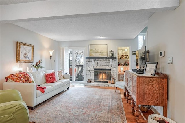 living room featuring plenty of natural light, a stone fireplace, wood-type flooring, and a textured ceiling