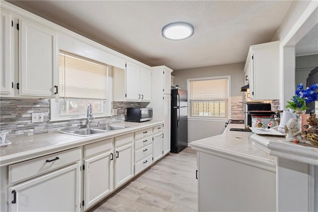 6133 Swope Pkwy, Kansas City, MO 64132 - kitchen with black refrigerator, sink, white cabinets, and light wood-type flooring