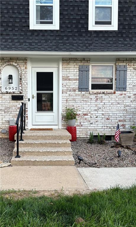 entrance to property with a shingled roof, brick siding, and mansard roof