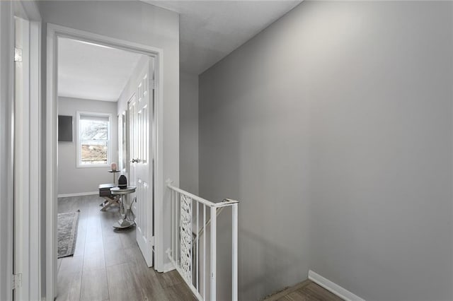 corridor with baseboards, an upstairs landing, and wood finished floors