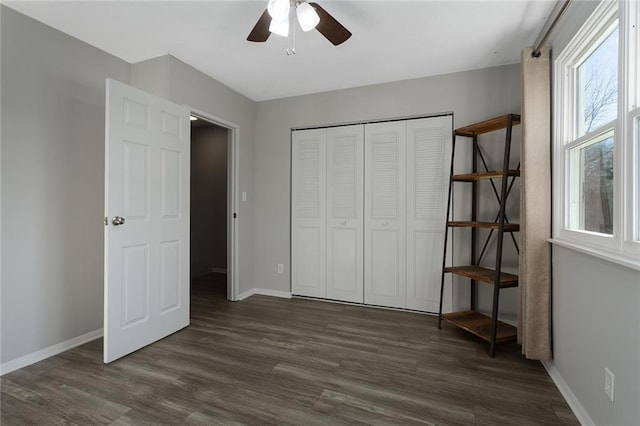 unfurnished bedroom featuring a closet, dark wood-style flooring, ceiling fan, and baseboards