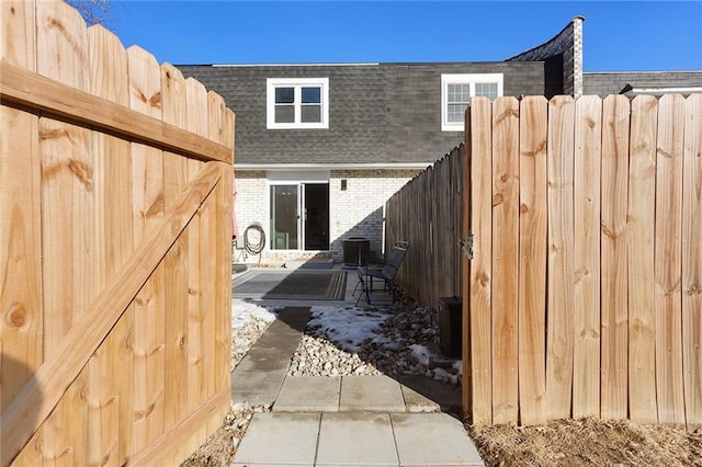 exterior space with mansard roof, roof with shingles, fence, cooling unit, and brick siding