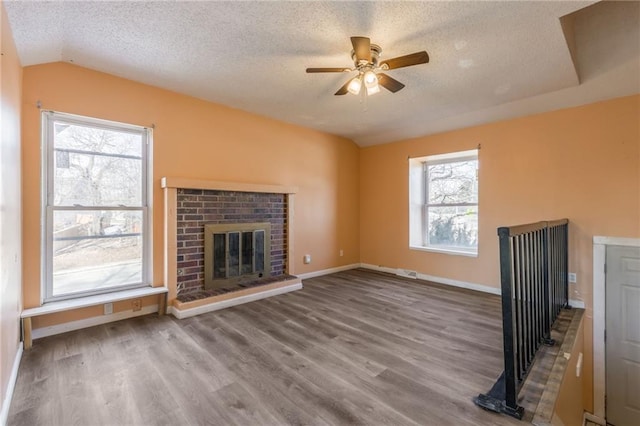 unfurnished living room featuring ceiling fan, wood-type flooring, a textured ceiling, a brick fireplace, and vaulted ceiling