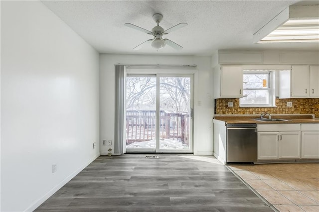 kitchen with stainless steel dishwasher, a textured ceiling, decorative backsplash, and white cabinets