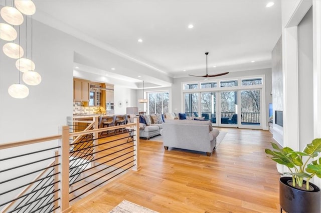 living room with crown molding, ceiling fan, and light wood-type flooring