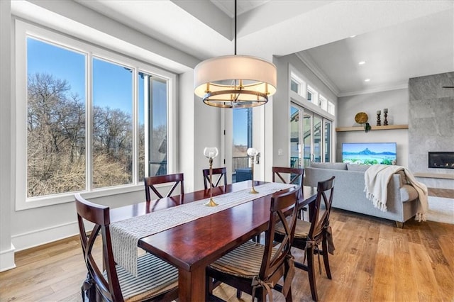 dining area with crown molding, a notable chandelier, a tile fireplace, and light wood-type flooring