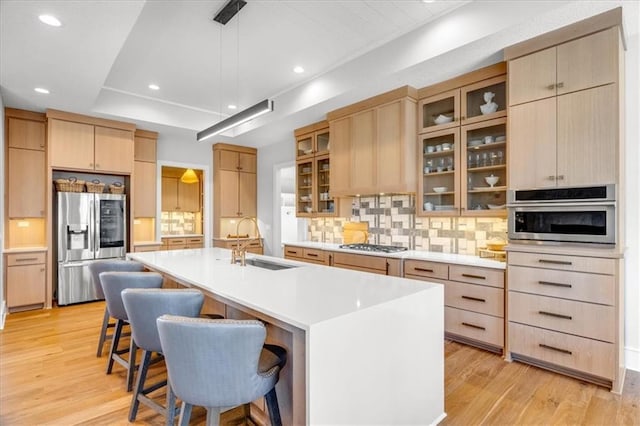 kitchen featuring sink, appliances with stainless steel finishes, light brown cabinets, an island with sink, and light wood-type flooring