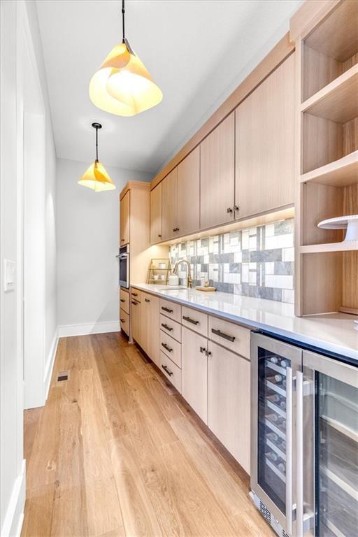 kitchen featuring sink, light hardwood / wood-style flooring, hanging light fixtures, light brown cabinets, and beverage cooler