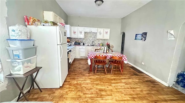 kitchen featuring white cabinetry, backsplash, white refrigerator, and light wood-type flooring