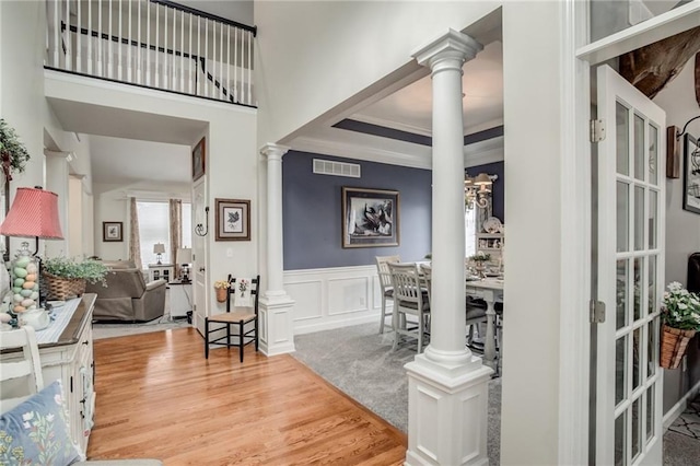 foyer entrance featuring wood finished floors, visible vents, ornate columns, wainscoting, and a decorative wall