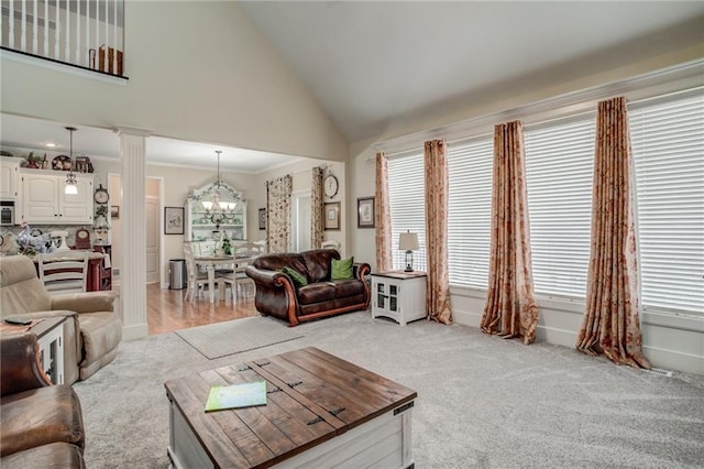 living room with crown molding, decorative columns, light carpet, an inviting chandelier, and high vaulted ceiling