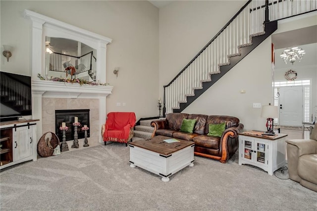 living room with a tiled fireplace, carpet flooring, stairway, and a towering ceiling