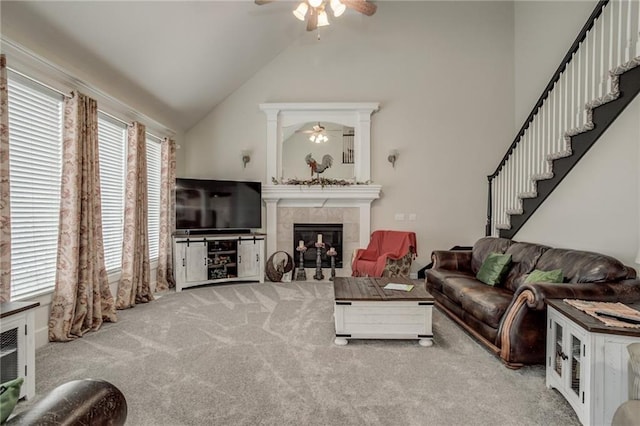 living area featuring a tiled fireplace, stairs, carpet flooring, high vaulted ceiling, and a ceiling fan