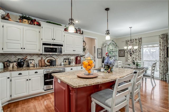 kitchen with light stone counters, a kitchen island, crown molding, light wood-style floors, and stainless steel microwave