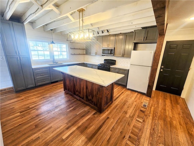 kitchen featuring a kitchen island, hanging light fixtures, white fridge, light stone counters, and black gas stove