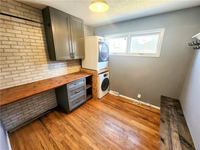 clothes washing area featuring stacked washing maching and dryer, a textured ceiling, and light wood-type flooring