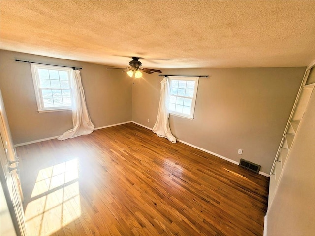 empty room featuring ceiling fan, hardwood / wood-style floors, a textured ceiling, and a wealth of natural light