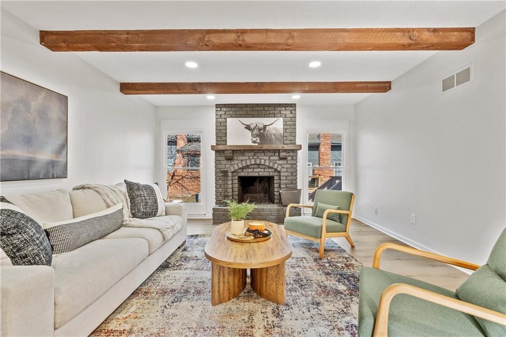 living room with hardwood / wood-style flooring, a brick fireplace, and beamed ceiling