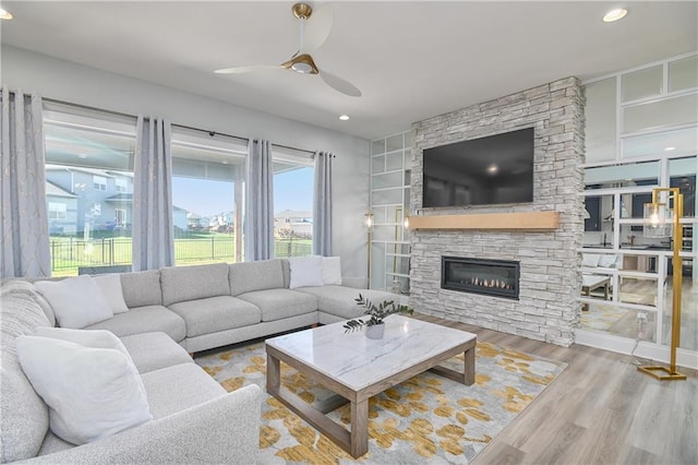 living room featuring ceiling fan, a stone fireplace, hardwood / wood-style floors, and built in features