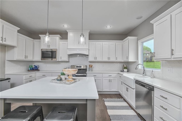 kitchen with appliances with stainless steel finishes, pendant lighting, white cabinetry, sink, and dark hardwood / wood-style flooring