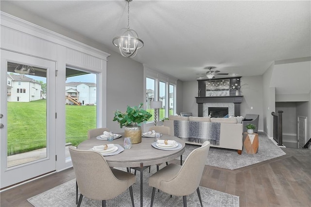 dining area with dark hardwood / wood-style floors, ceiling fan with notable chandelier, a large fireplace, and a healthy amount of sunlight