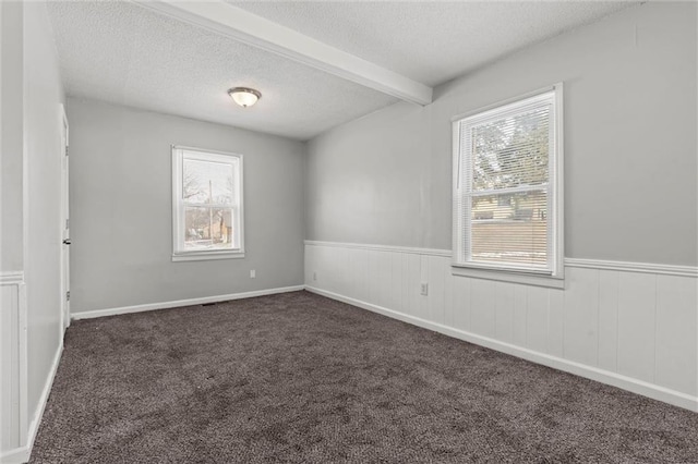 empty room with beamed ceiling, dark carpet, and a textured ceiling