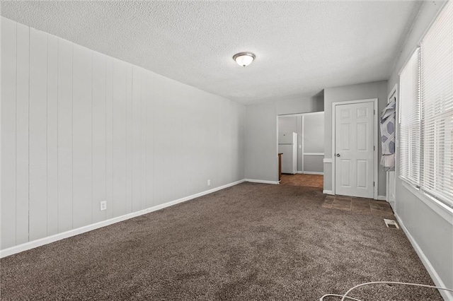 unfurnished bedroom featuring white fridge, a textured ceiling, and dark colored carpet