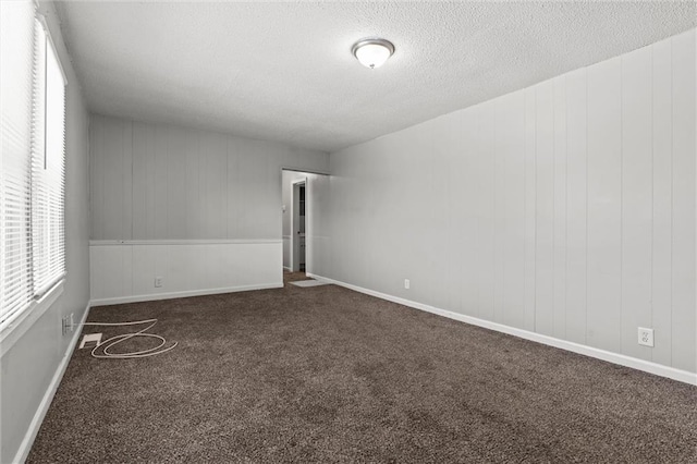 carpeted spare room featuring wooden walls and a textured ceiling