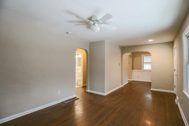 unfurnished room with a ceiling fan, baseboards, arched walkways, and wood finished floors