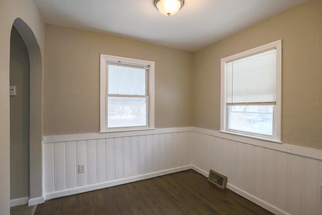 empty room with dark wood-type flooring, arched walkways, a wainscoted wall, and visible vents