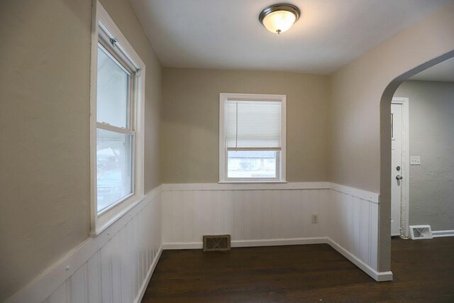 unfurnished room featuring arched walkways, dark wood-style flooring, visible vents, and wainscoting