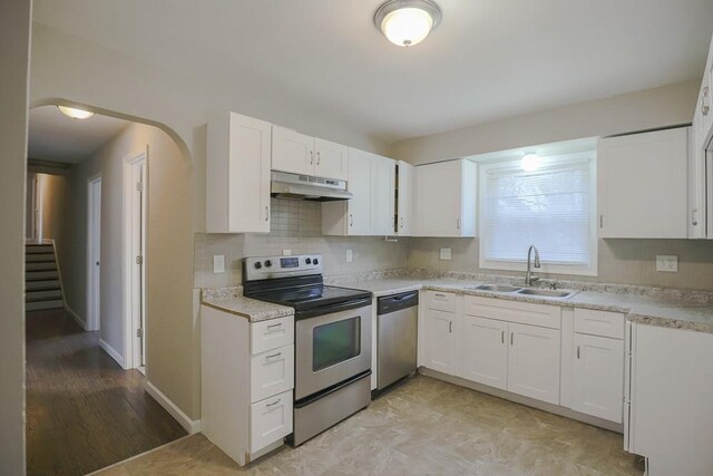 kitchen with appliances with stainless steel finishes, light countertops, a sink, and under cabinet range hood