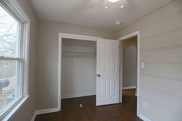 unfurnished bedroom with a closet, baseboards, and dark wood-type flooring