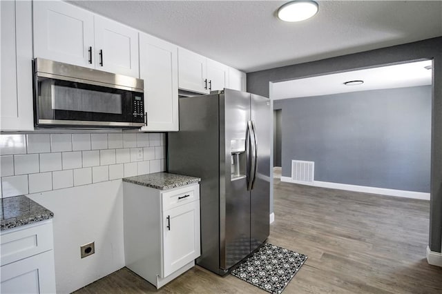 kitchen with stainless steel appliances, hardwood / wood-style floors, dark stone countertops, and white cabinets