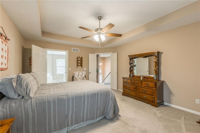 bedroom with light carpet, ensuite bath, a raised ceiling, and ceiling fan